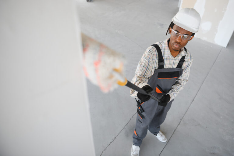 African american construction worker painting walls with roller brush in a building under construction